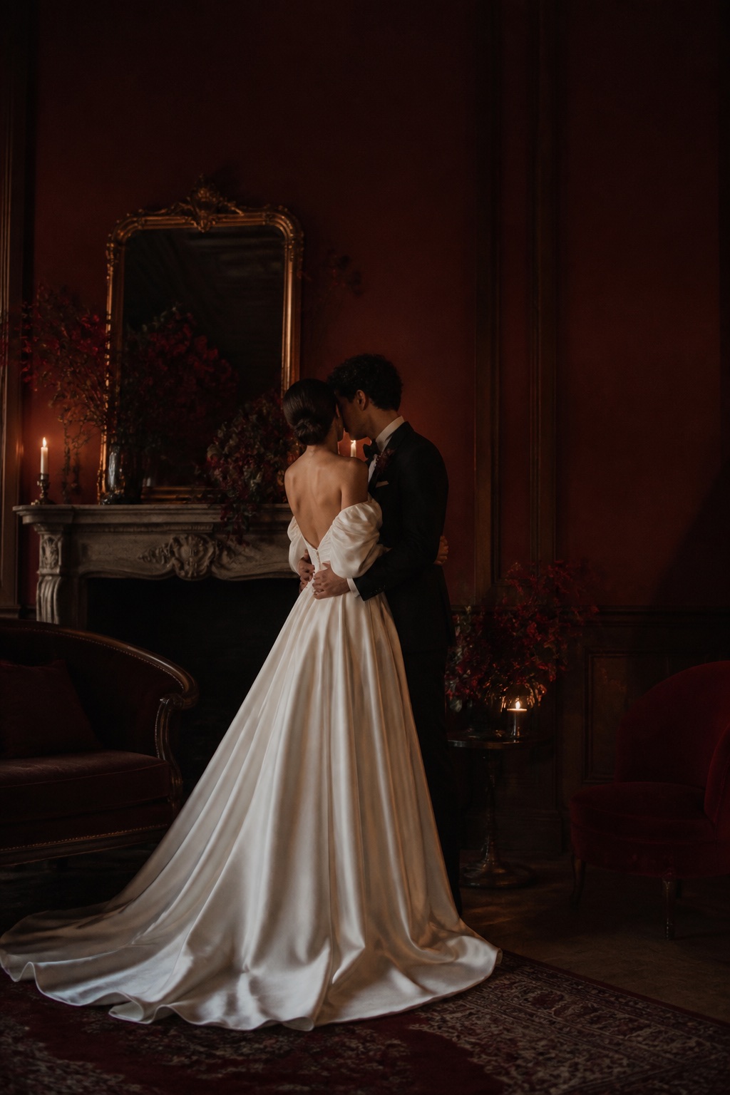 A newlywed couple in a candlelit burgundy salon