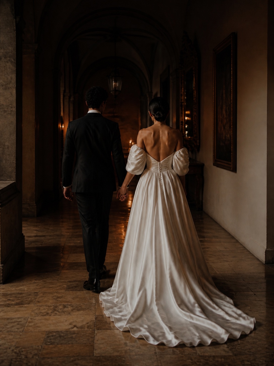 A newlywed couple walking through a historic corridor